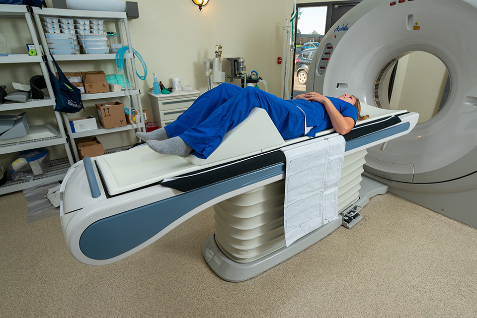 A photo of a person laying down on an MRI machine with their knees elevated using a wedge.