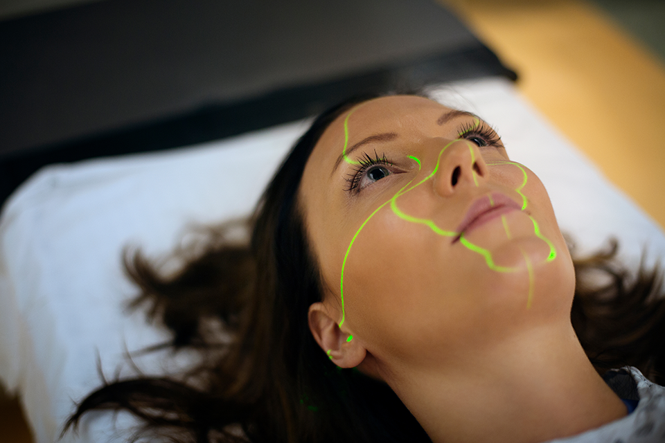 A close-up photo of a woman laying on a MRI machine with light being projected onto her face.