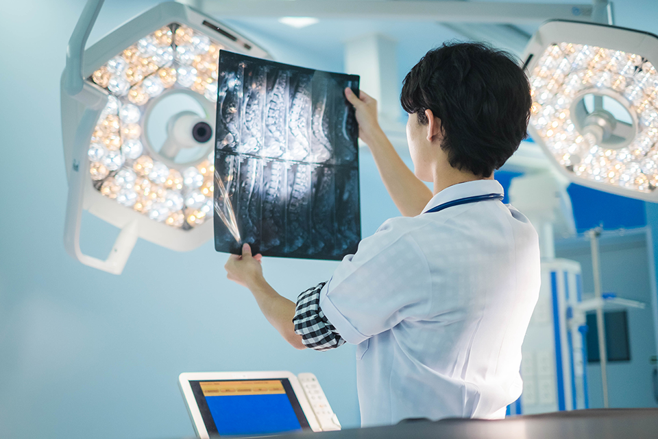 A photo of a person looking at an X-ray with their back turned to the camera.