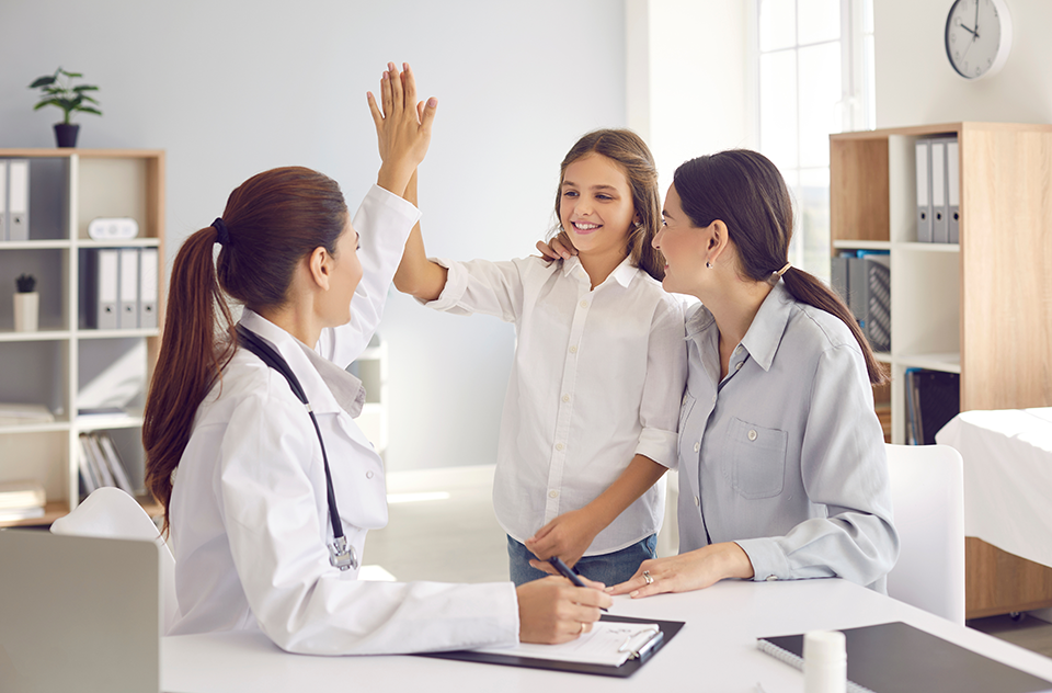 A photo of a doctor high-fiving a pediatric patient while her mother looks at her.