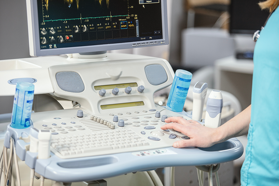 Close up of a modern ultrasound machine with a doctor visible in the edge of the frame.